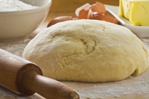 Dough on wooden board with rolling pin.